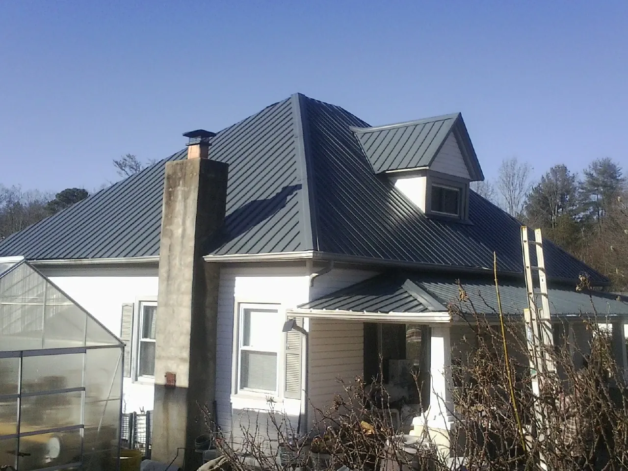 Dark blue standing seam metal roof on a white farmhouse with dormer — Slate & Tile Roof Repair by Roofing Brothers in Moscow